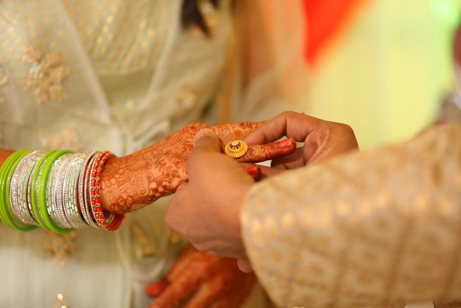 Close-up of a couple exchanging rings with intricate mehendi and colorful bangles, highlig